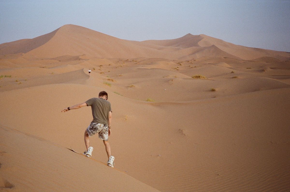 A guest sandboarding down a dune in twilight light