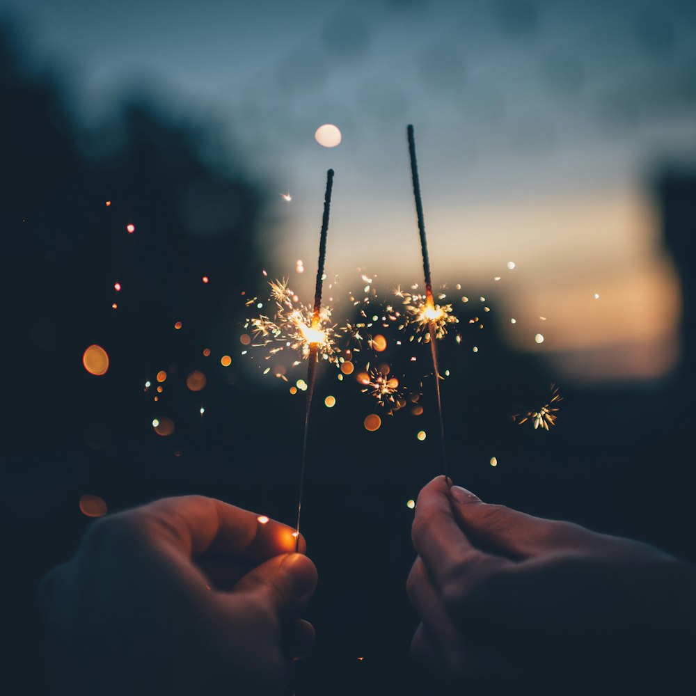 Two hands holding sparklers together at dusk